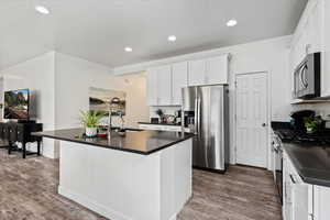 Kitchen featuring wood-type flooring, appliances with stainless steel finishes, white cabinetry, and an island with sink