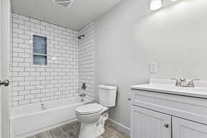 Full bathroom in basement featuring vanity, tiled shower / bath combo, and toilet