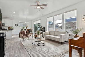 Living room with ceiling fan with notable chandelier, light wood-type flooring, and sink