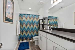 Bathroom with tile flooring, vanity, toilet, quartz countertops, and a shower with shower curtain