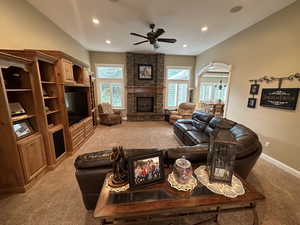 Carpeted living room with ceiling fan and stone fireplace.