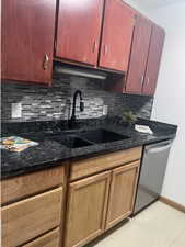 Kitchen with sink, stainless steel dishwasher, backsplash, and dark stone counters