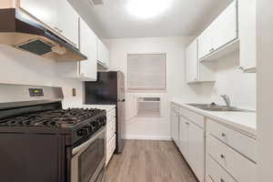 Kitchen with white cabinetry, sink, light hardwood / wood-style floors, a textured ceiling, and appliances with stainless steel finishes