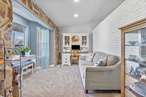 Living area with light colored carpet, brick wall, vaulted ceiling, built in desk, and recessed lighting