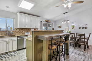 Kitchen featuring a center island, sink, stainless steel dishwasher, lofted ceiling, and white cabinets