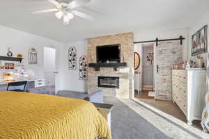 Carpeted bedroom with a barn door, ceiling fan, and a fireplace