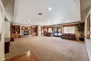 Unfurnished living room featuring carpet, a stone fireplace, and a textured ceiling