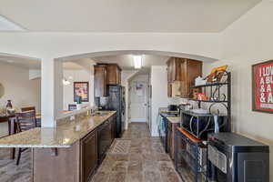 Kitchen featuring a breakfast bar, sink, light stone counters, kitchen peninsula, and stainless steel appliances