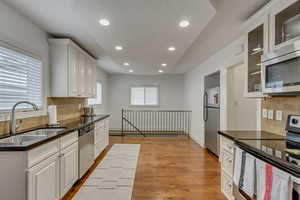 Kitchen with light wood-type flooring, appliances with stainless steel finishes, decorative backsplash, sink, and white cabinets