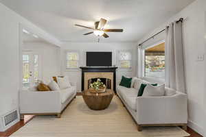 Living room with a tiled fireplace, a wealth of natural light, ceiling fan, and light hardwood / wood-style flooring