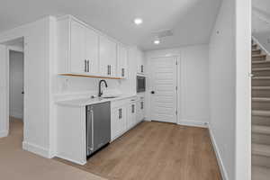 Kitchen with stainless steel appliances, sink, white cabinets, and light hardwood / wood-style floors