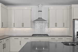 Kitchen with decorative backsplash, white cabinetry, wall chimney exhaust hood (work in progress), and stainless steel appliances