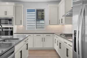 Kitchen with white cabinets, light hardwood / wood-style floors, wall chimney range hood, and stainless steel appliances