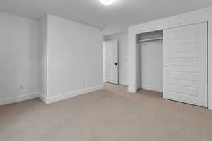 Unfurnished bedroom with light colored carpet, a textured ceiling, and a closet