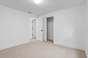 Unfurnished bedroom featuring light carpet, a textured ceiling, and a closet