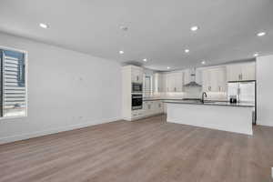 Kitchen featuring white cabinets, wall chimney exhaust hood (work in progress),, light wood-type flooring, and stainless steel appliances