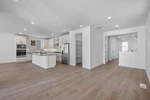 Kitchen with stainless steel appliances, wall chimney range hood, light hardwood / wood-style flooring, white cabinets, and a center island