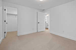 Unfurnished bedroom with a walk in closet, a closet, light colored carpet, and a textured ceiling