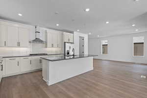 Kitchen with light hardwood / wood-style floors, stainless steel appliances, wall chimney exhaust hood (work in progress),, and a kitchen island with sink