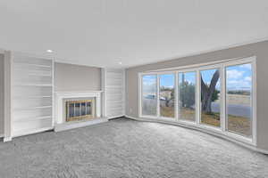 Unfurnished living room with built in features, a fireplace, carpet, and a textured ceiling