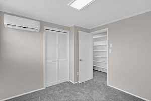 Unfurnished bedroom featuring a textured ceiling, carpet, a wall mounted air conditioner, and ornamental molding