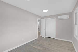 Unfurnished bedroom featuring light wood-type flooring, an AC wall unit, and a closet