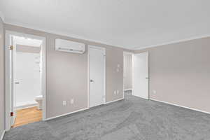 Unfurnished bedroom with ensuite bathroom, carpet floors, a textured ceiling, and a wall mounted AC