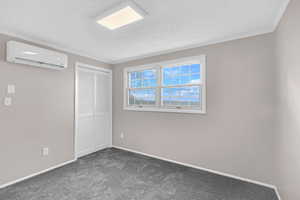 Unfurnished bedroom with a wall mounted air conditioner, dark colored carpet, a textured ceiling, a closet, and ornamental molding