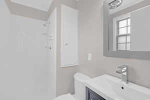 Bathroom with vanity, toilet, a tile shower, and ornamental molding