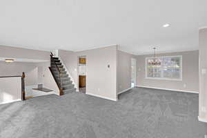 Unfurnished living room featuring a notable chandelier, carpet floors, and ornamental molding