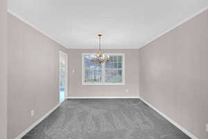 Unfurnished room featuring carpet, ornamental molding, a textured ceiling, and a notable chandelier