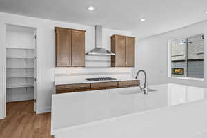 Kitchen featuring sink, wall chimney exhaust hood, light hardwood / wood-style floors, stainless steel gas stovetop, and a center island with sink