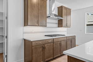 Kitchen with decorative backsplash, light wood-type flooring, stainless steel gas stovetop, and wall chimney exhaust hood