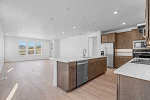 Kitchen featuring appliances with stainless steel finishes, extractor fan, sink, a center island with sink, and light hardwood / wood-style flooring