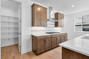 Kitchen featuring stainless steel gas stovetop, wall chimney exhaust hood, light wood-type flooring, and backsplash