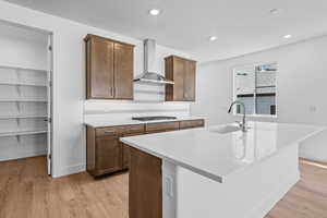 Kitchen with wall chimney range hood, sink, light hardwood / wood-style flooring, an island with sink, and stainless steel gas cooktop