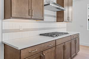 Kitchen featuring tasteful backsplash, light hardwood / wood-style floors, wall chimney range hood, and stainless steel gas stovetop