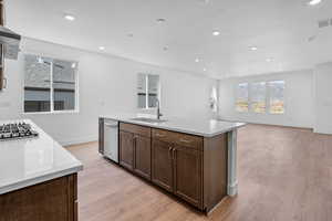 Kitchen featuring a kitchen island with sink, sink, appliances with stainless steel finishes, and light wood-type flooring