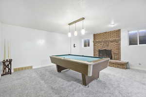 Recreation room with light carpet, pool table, a textured ceiling, and a brick fireplace