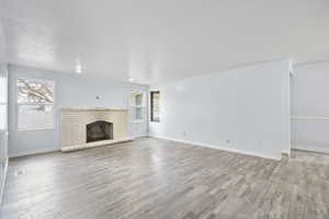 Unfurnished living room with a brick fireplace, a textured ceiling, and light hardwood / wood-style flooring