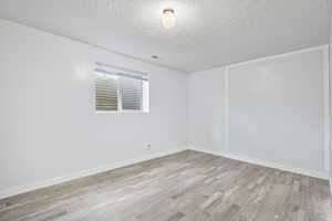 Unfurnished room with a textured ceiling and light hardwood / wood-style floors