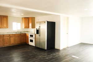 Kitchen with white stove, dark hardwood / wood-style flooring, stainless steel fridge with ice dispenser, and sink