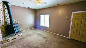 Unfurnished living room featuring dark colored carpet, a wood stove, and ceiling fan