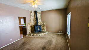 Unfurnished living room with carpet, a wood stove, sink, ceiling fan, and a textured ceiling