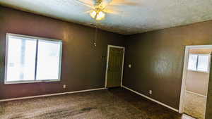 Unfurnished room with ceiling fan, a textured ceiling, and dark colored carpet