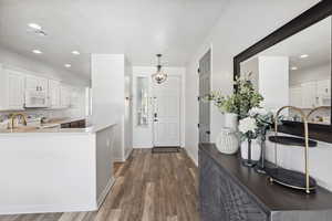 Kitchen featuring white cabinetry, kitchen peninsula, white appliances, dark wood-type flooring, and hanging light fixtures