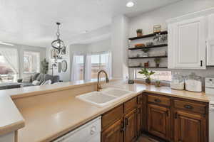 Kitchen featuring kitchen peninsula, white appliances, decorative light fixtures, a textured ceiling, and sink