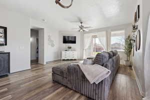 Living room with ceiling fan, dark wood-type flooring, and a textured ceiling