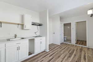 Kitchen with sink, white cabinets, exhaust hood, and light hardwood / wood-style flooring