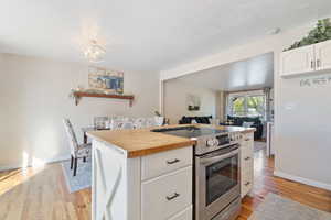 Kitchen with wood counters, light wood-type flooring, stainless steel electric stove, white cabinets, and hanging light fixtures